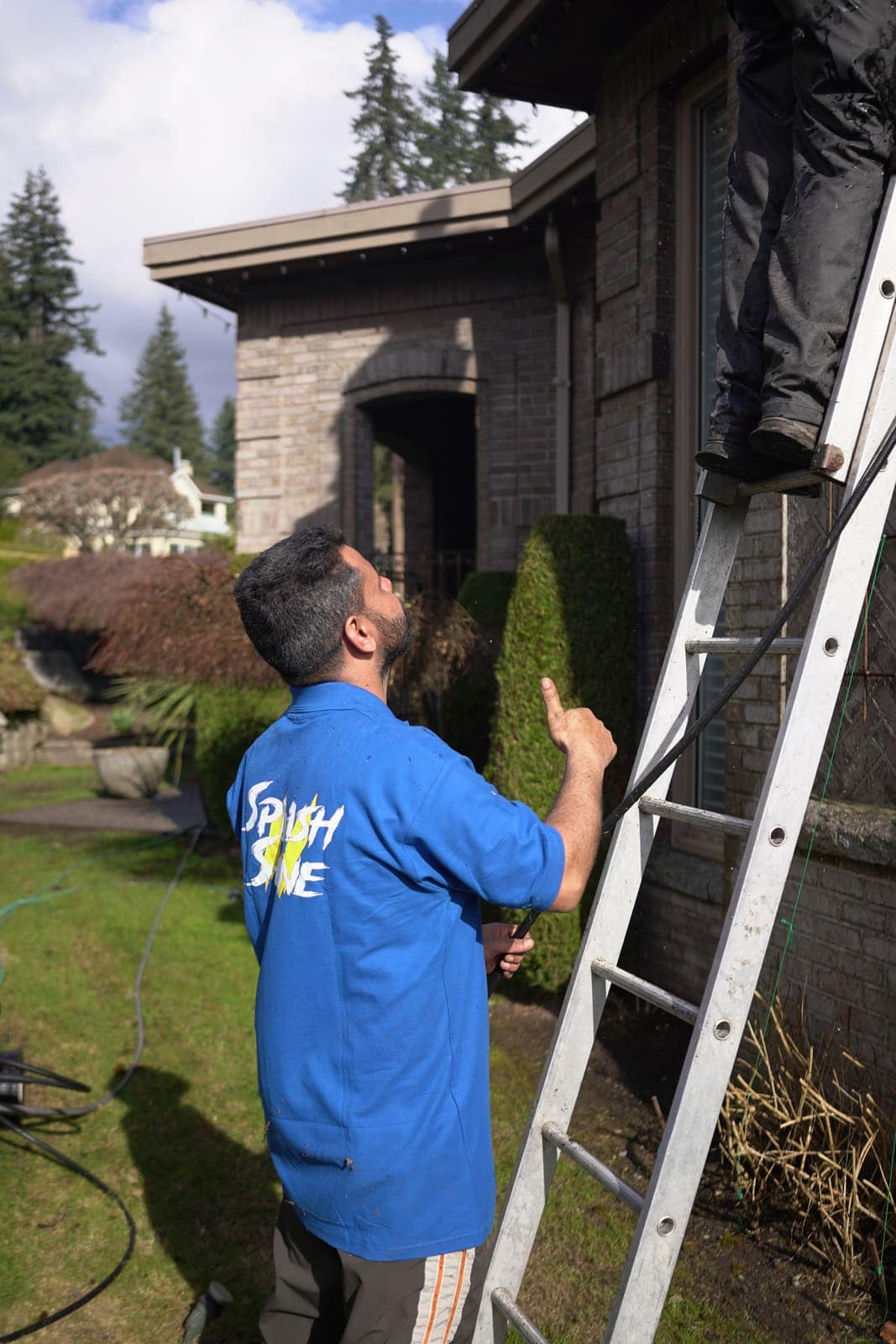 One technician foots the ladder while another climbs to the roof