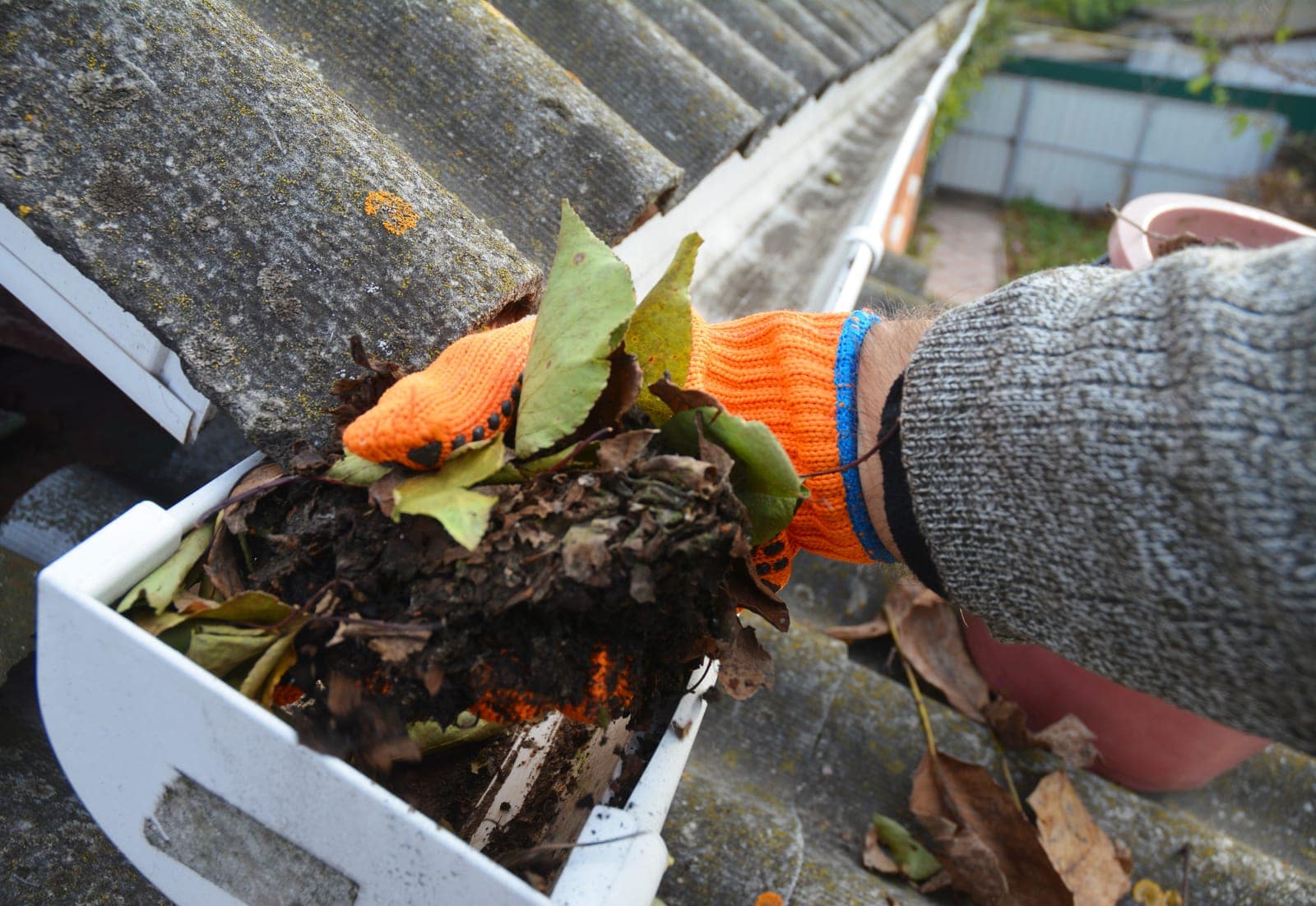 A gloved hand clearing built-up debris from a gutter