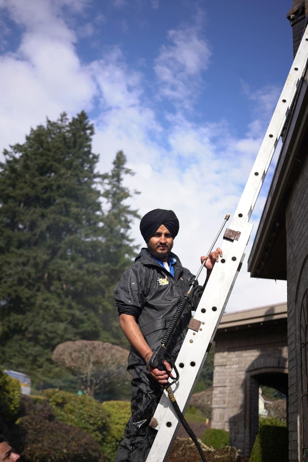 Technician steadying an extension ladder against a brick house