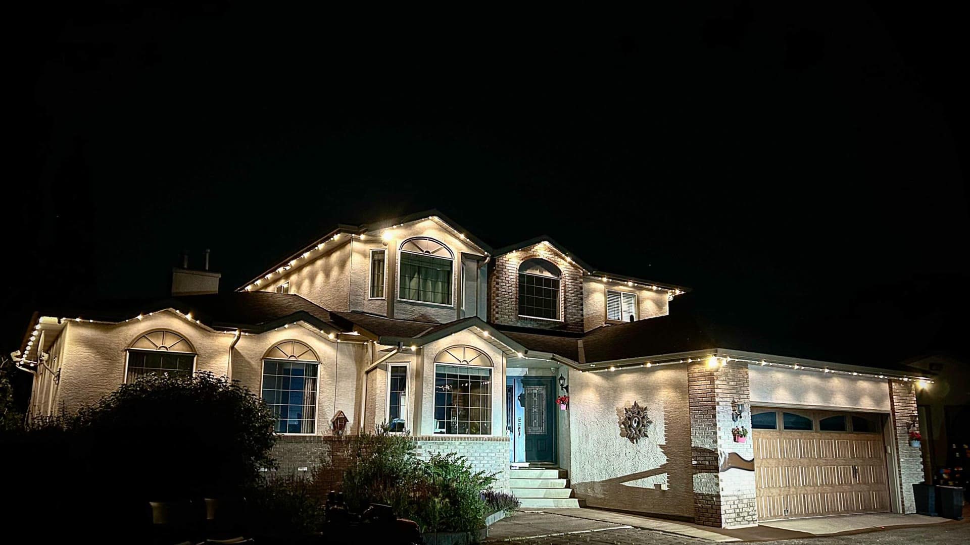 Two-storey home traced in warm-white permanent lights along the rooflines at dusk