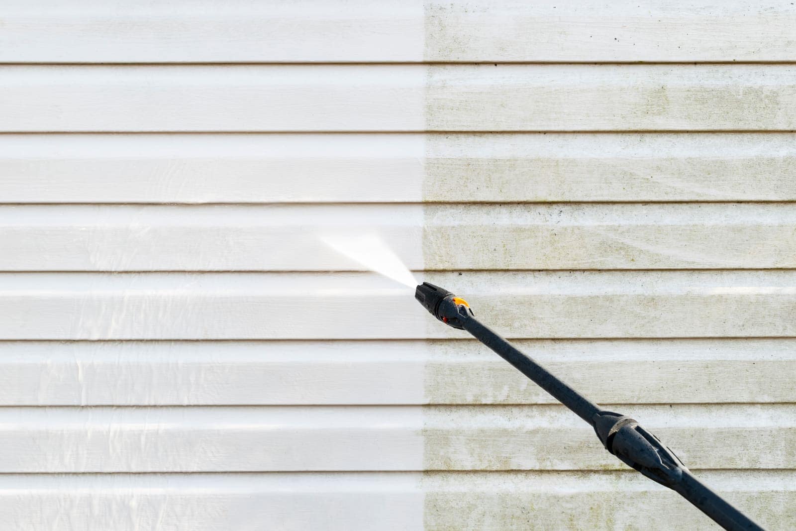 Siding wall half cleaned with a low-pressure wand, clean side sharply visible against grime