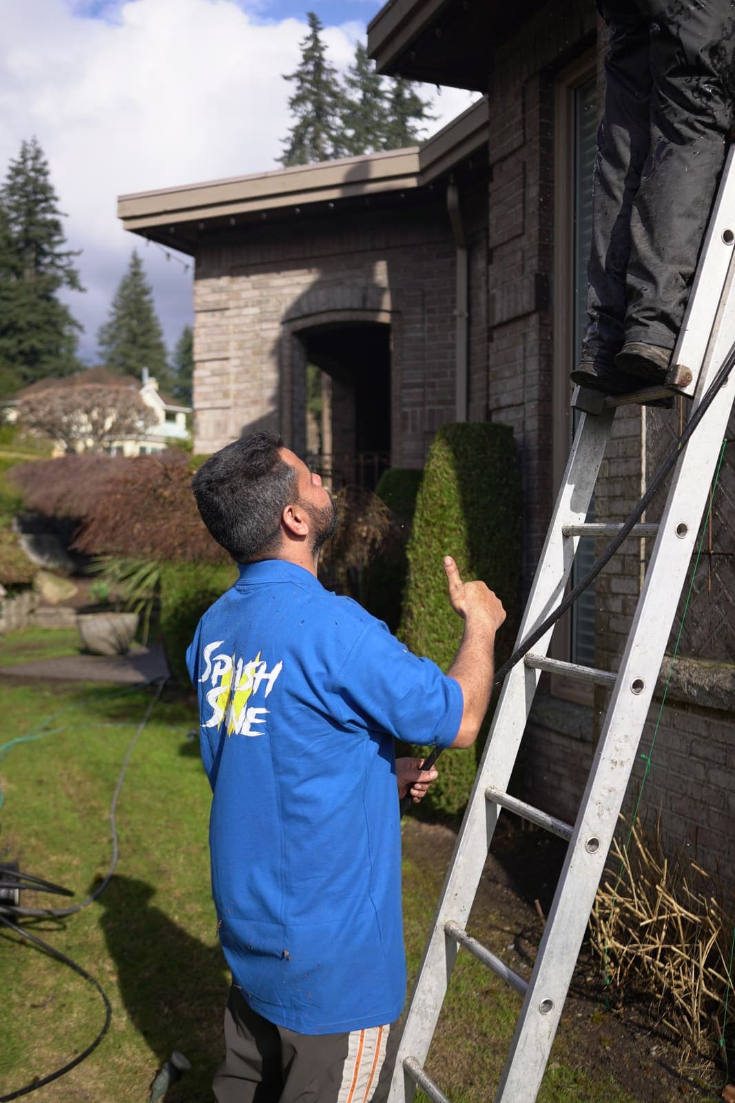 One technician foots the ladder while another climbs to the roof
