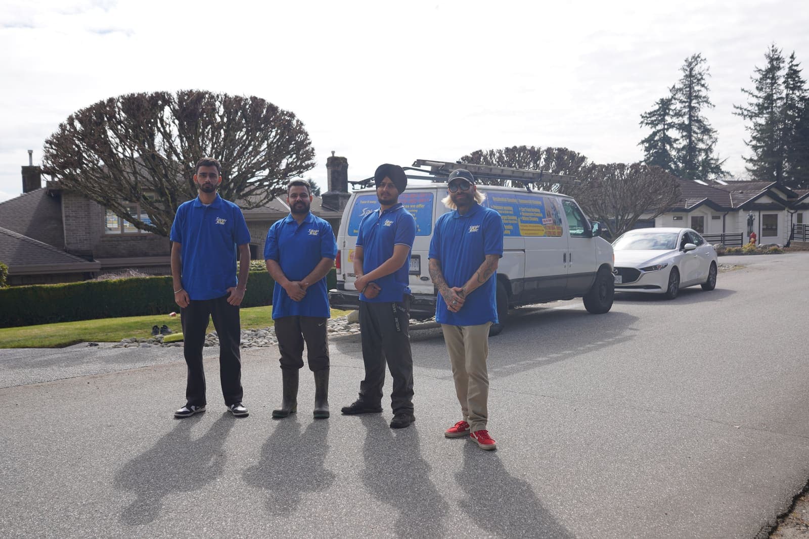 Four uniformed exterior cleaning technicians standing in front of the work van