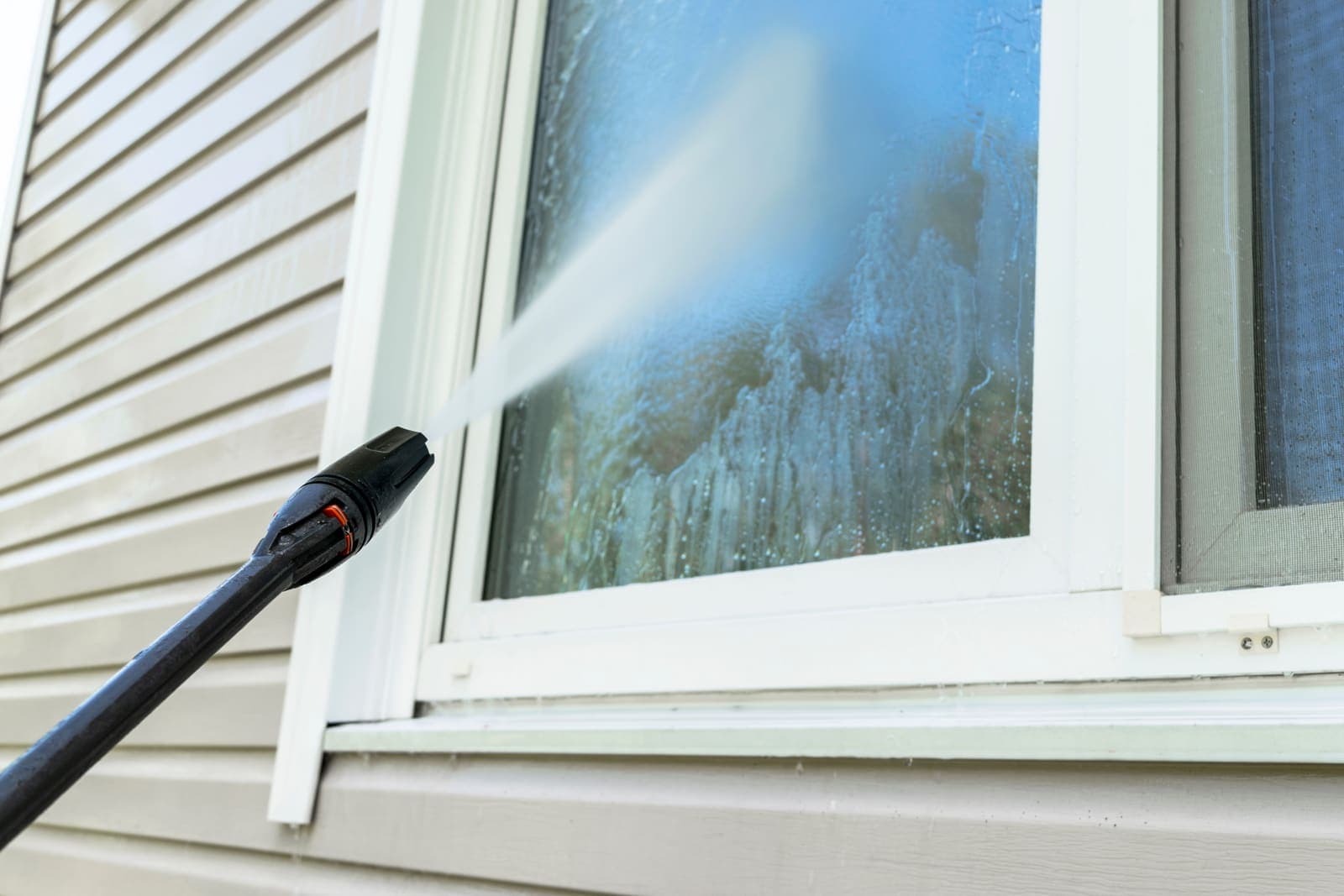 Low-pressure spray cleaning vinyl siding around a window