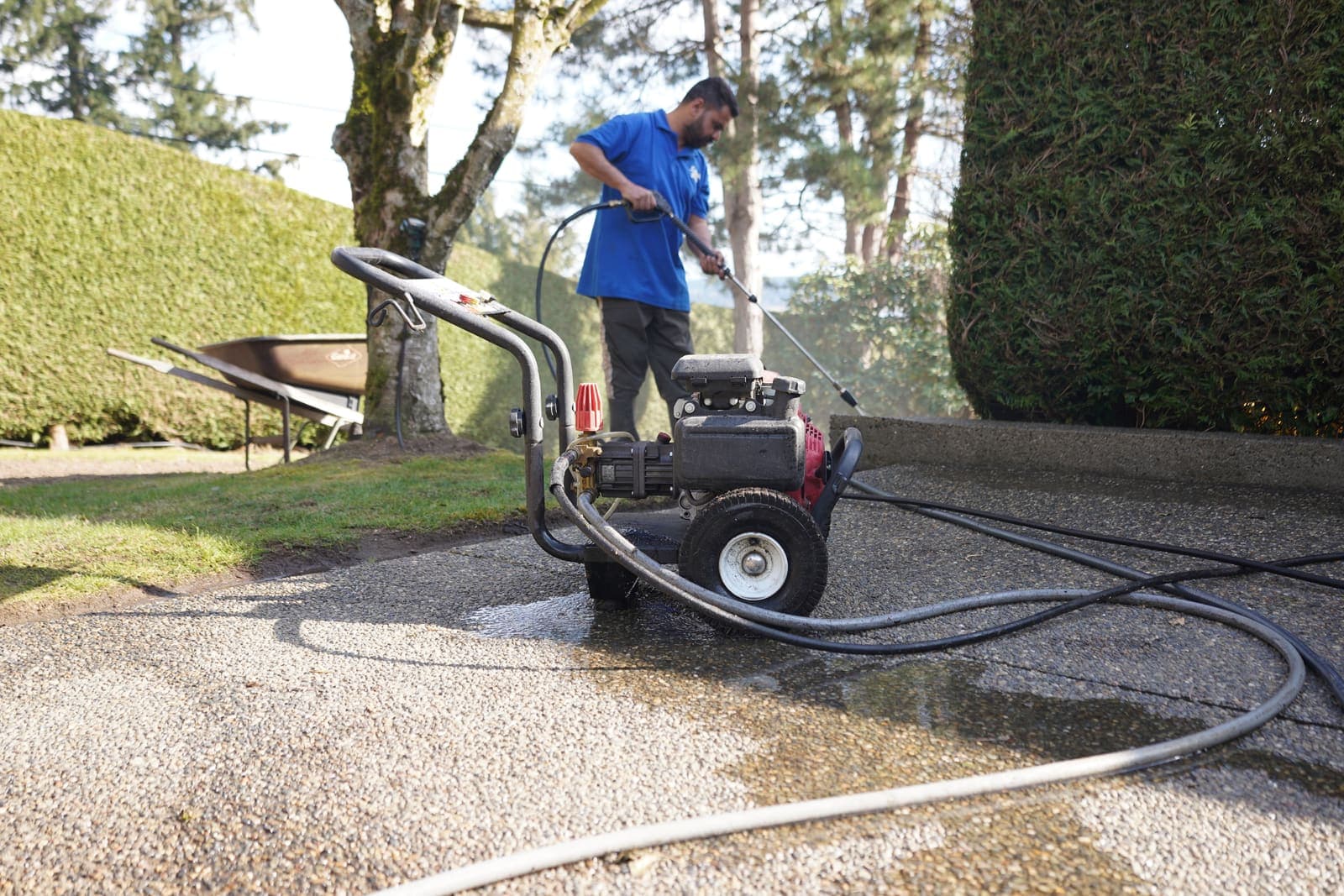 Technician working a pressure washer along a gravel and paver driveway