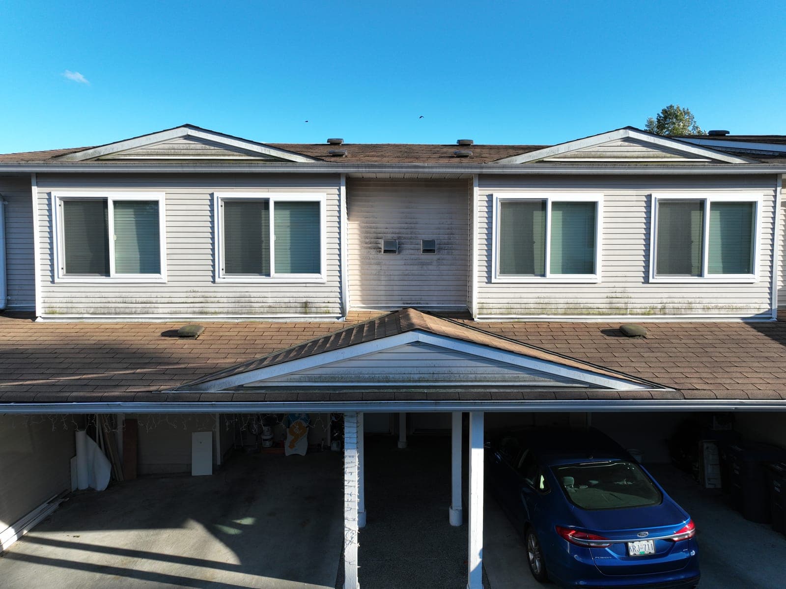 A weathered, moss-tinged townhouse roof and carport before cleaning