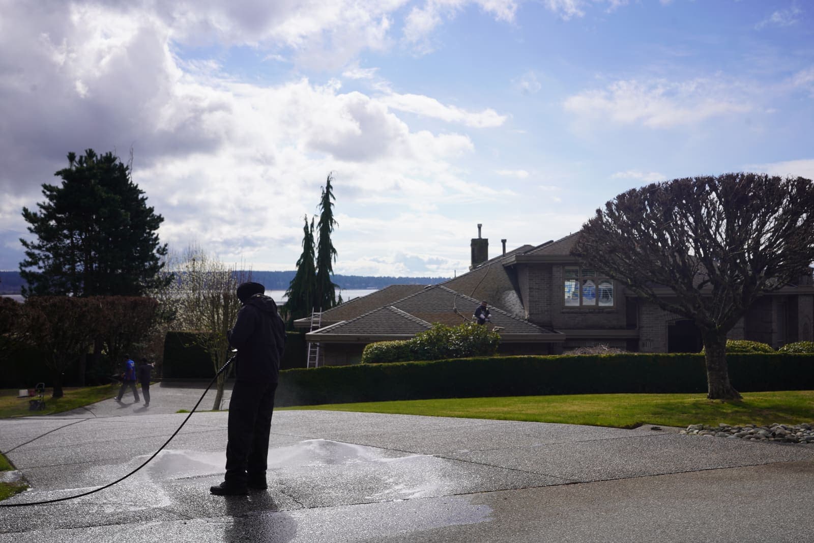 Technician washing a long estate driveway in front of a hedged property