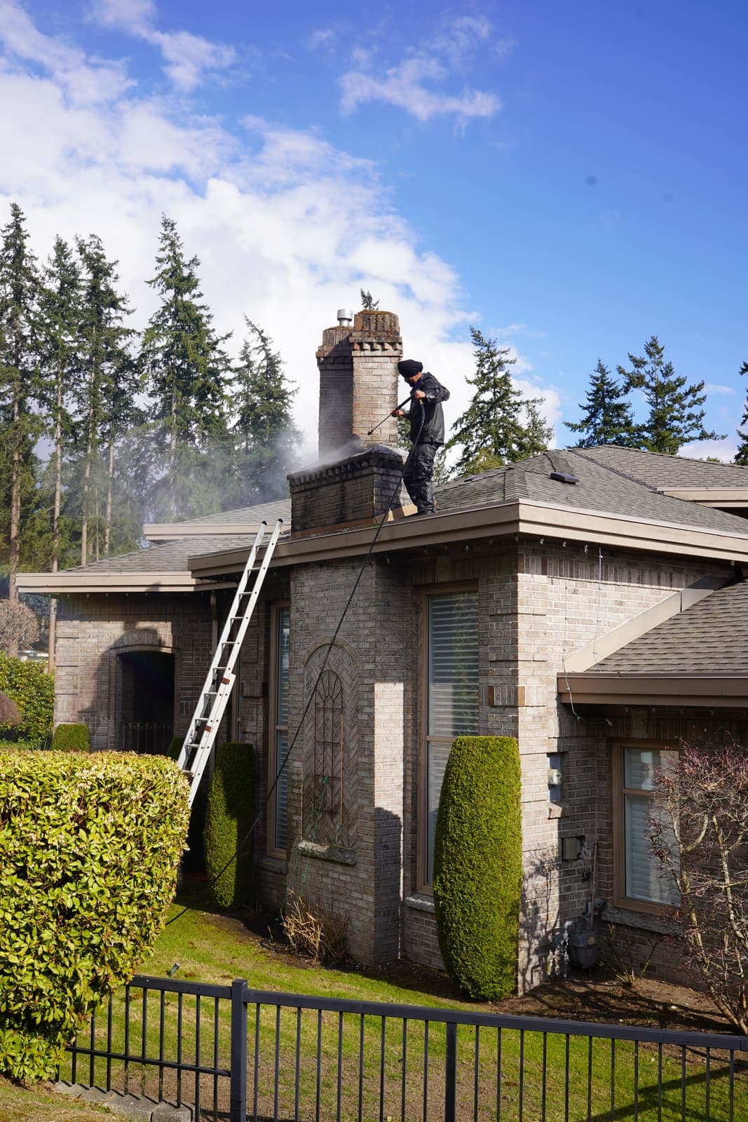 Worker moving across the roof of a stone-clad house during a cleaning job