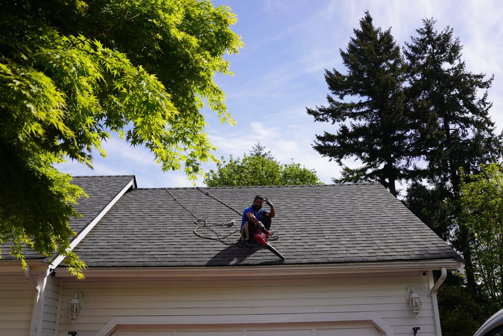 A worker pressure washing an asphalt shingle roof, a method that strips the protective granules
