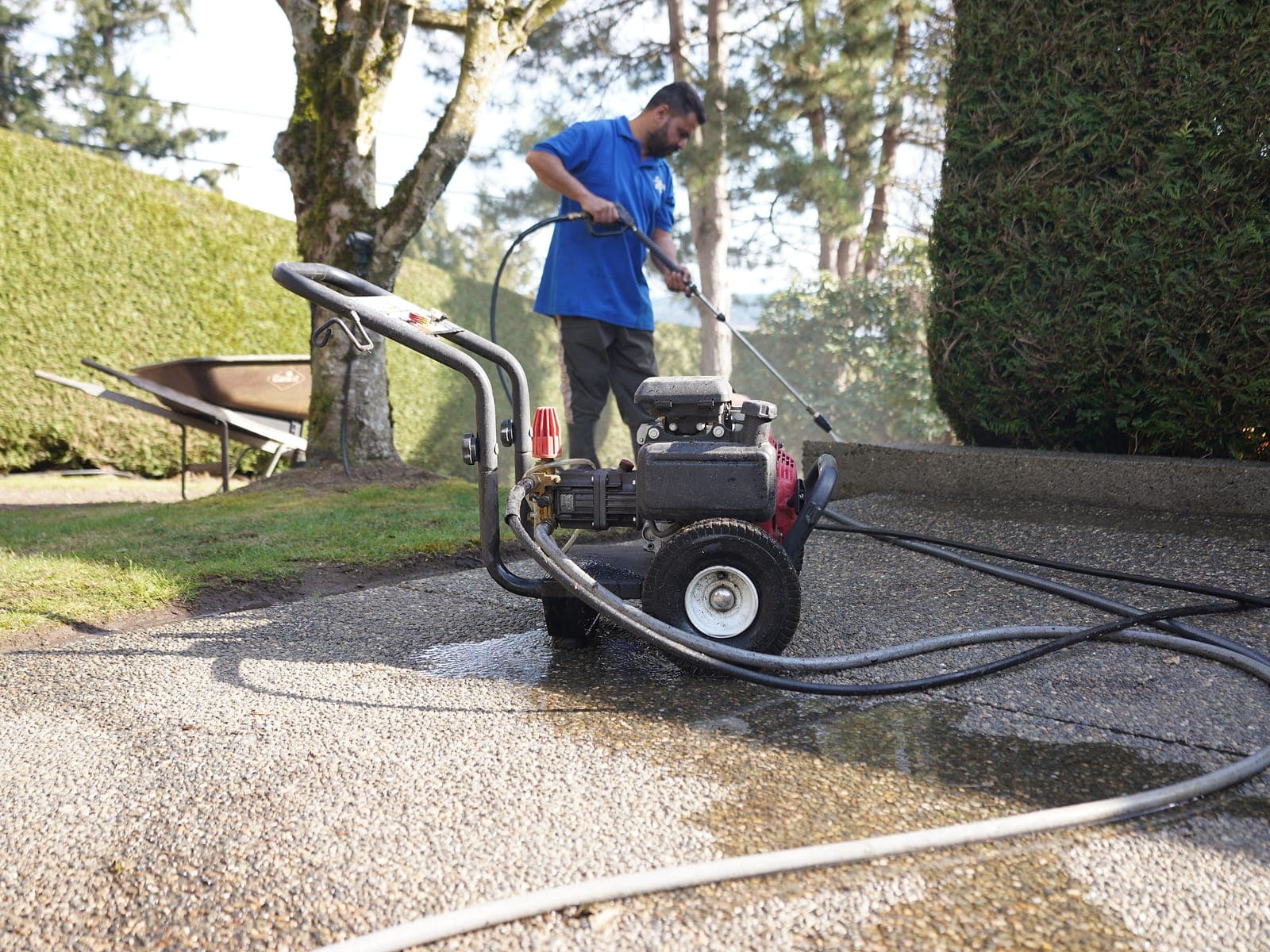 Rotary surface cleaner pressure washing a concrete driveway, showing the clean strip against dirty concrete