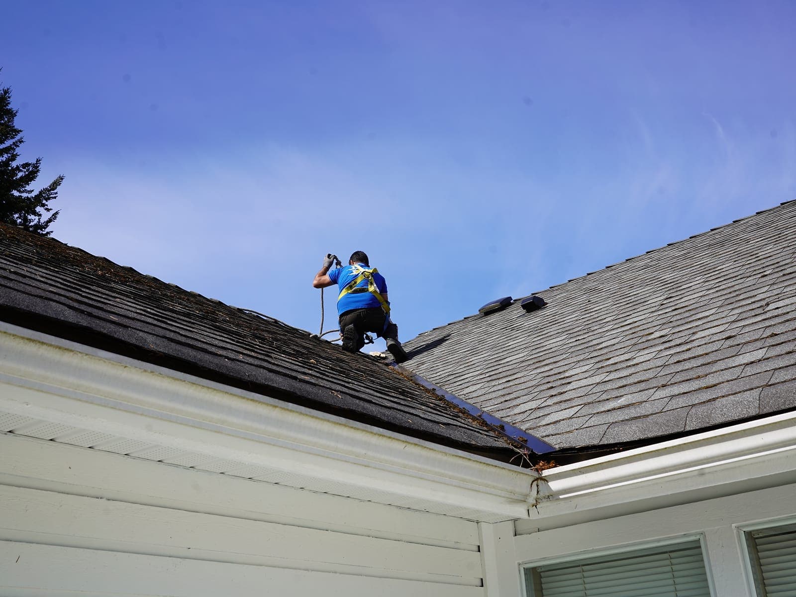 Technician clearing debris along a roof ridge with a blower during a professional roof cleaning