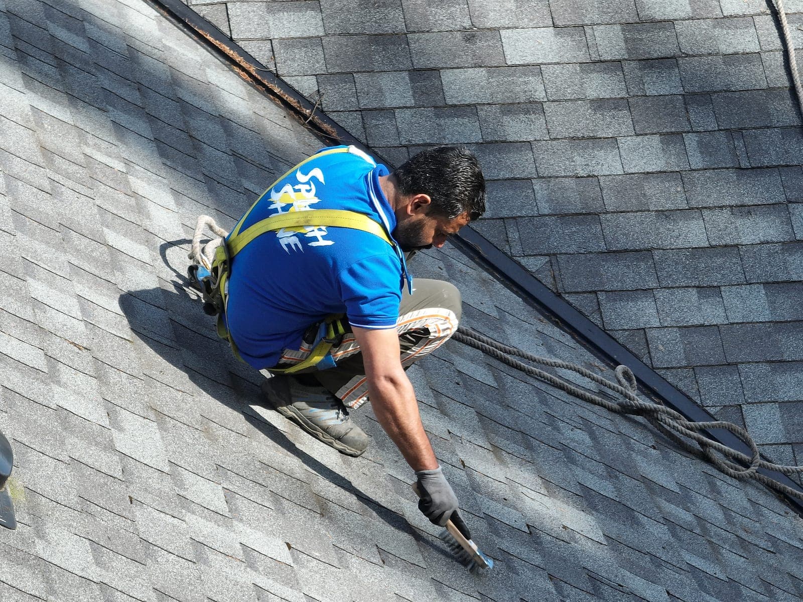 Technician in a safety harness working across a steep asphalt shingle roof during a roof cleaning